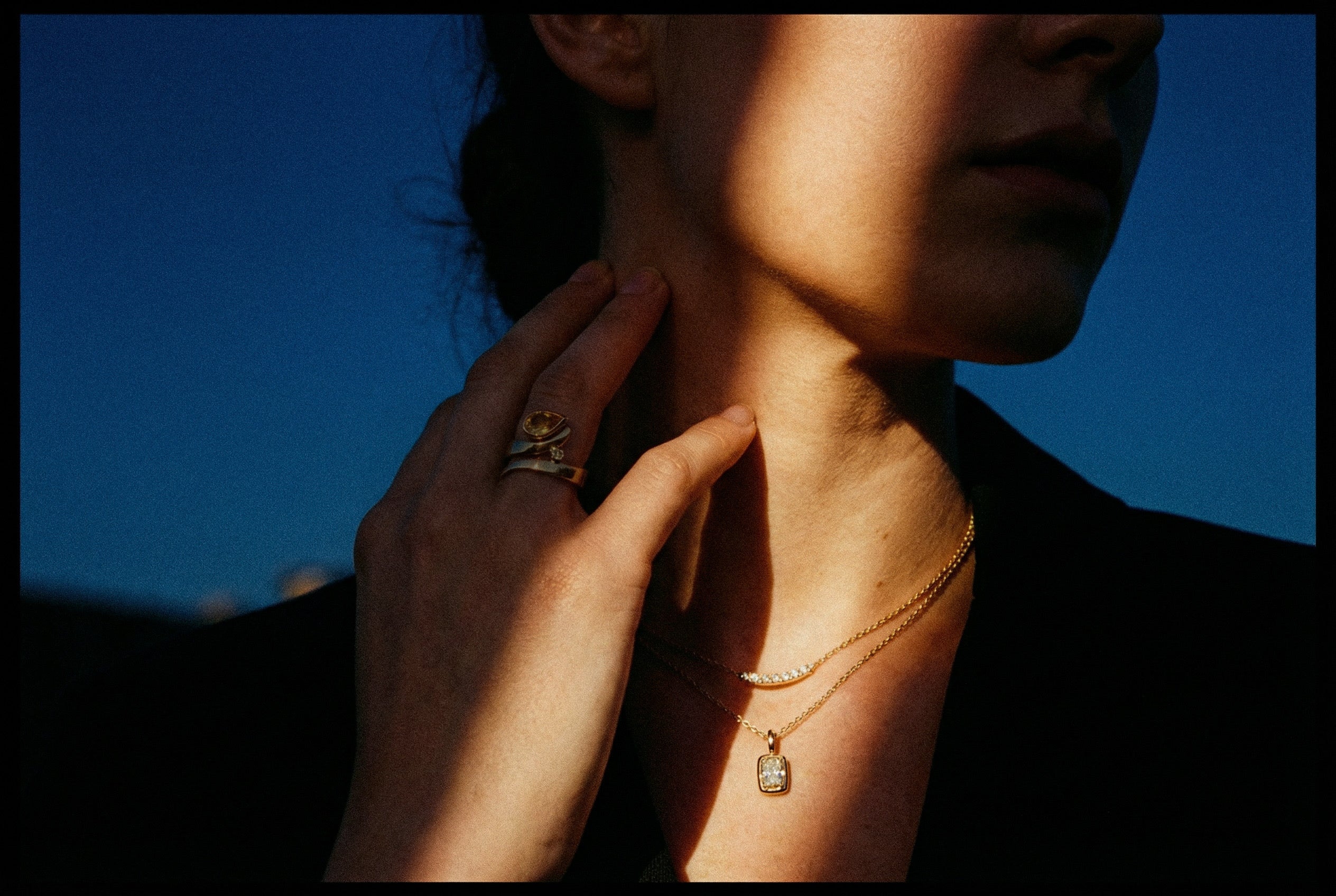 Close-up of a person wearing a gold necklace with a pendant against a blue background