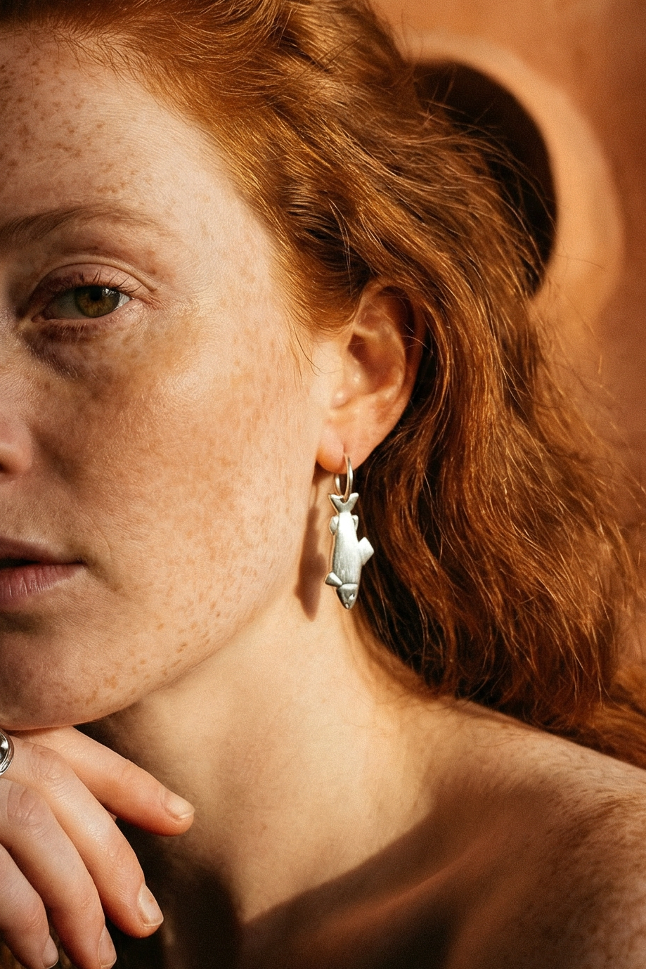 Woman with red hair and freckles against a warm-toned wall.